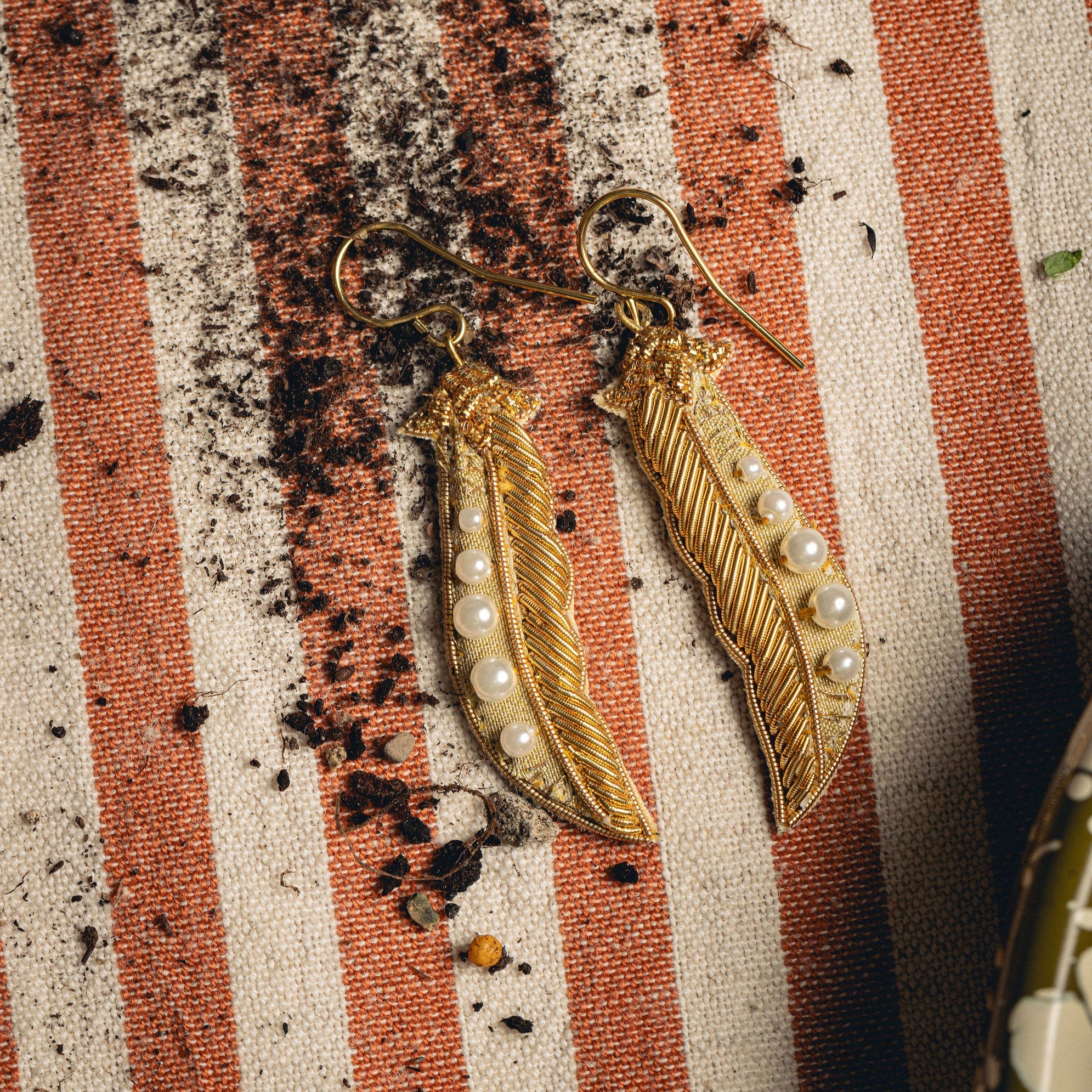 Golden Pea Earrings - Hand Embroidered earrings on a striped background with soil