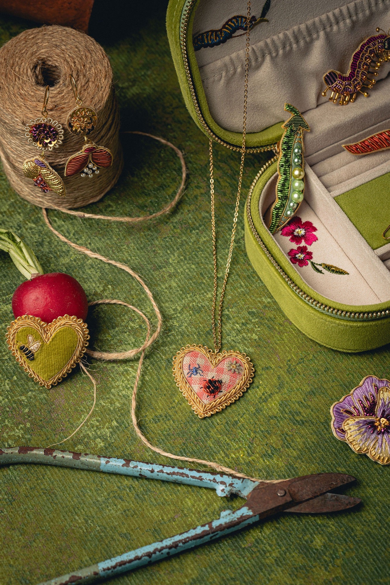 How Does Your Garden Grow? Collection of Hand Embroidered Jewellery - Brooches, earrings and a necklace shown on a green background with decorative props and a jewellery box