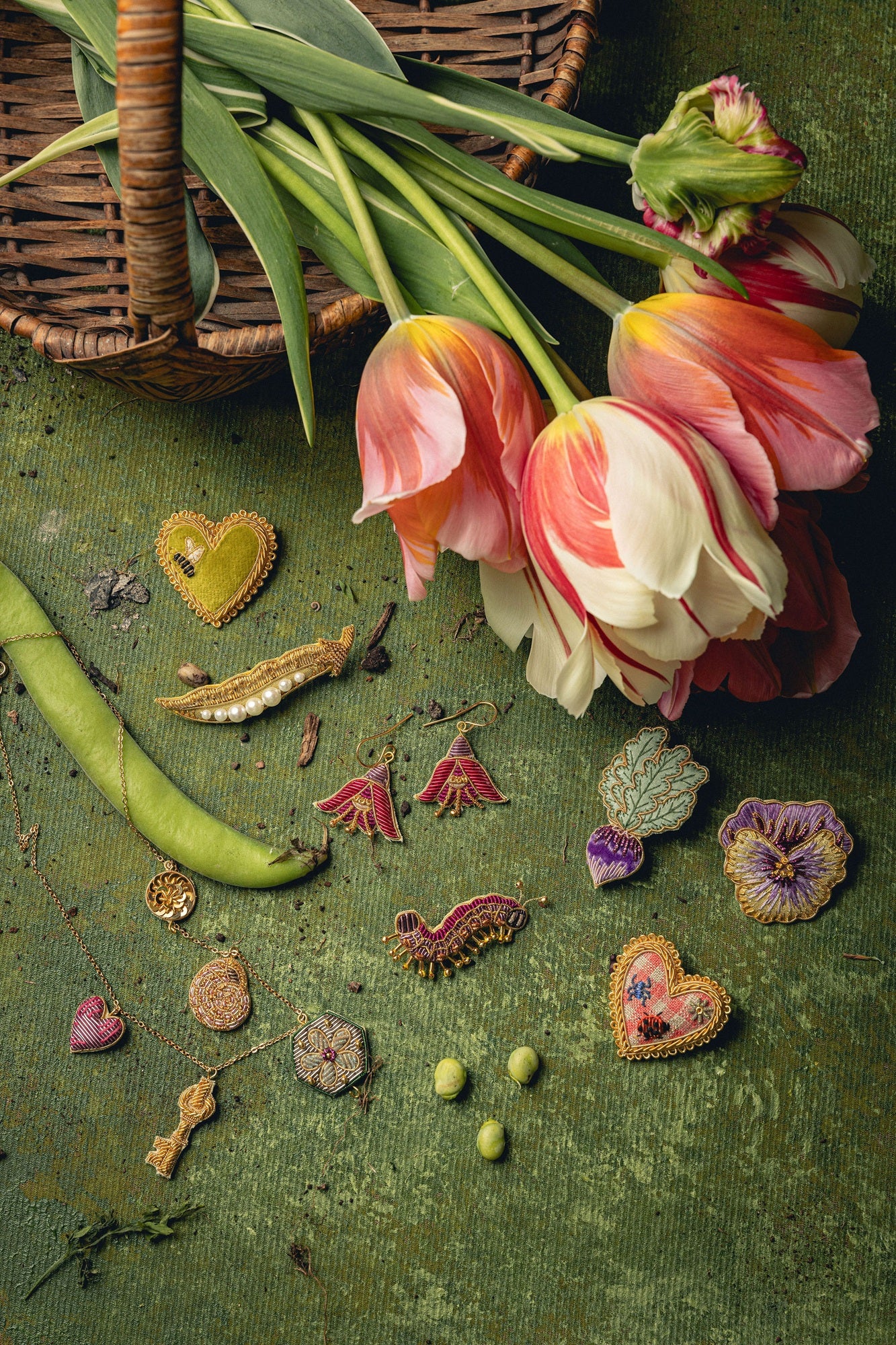 How Does Your Garden Grow? Collection of Hand Embroidered Jewellery - Selection of embroidered jewellery on a green background, with a basket of tulips and runner beans