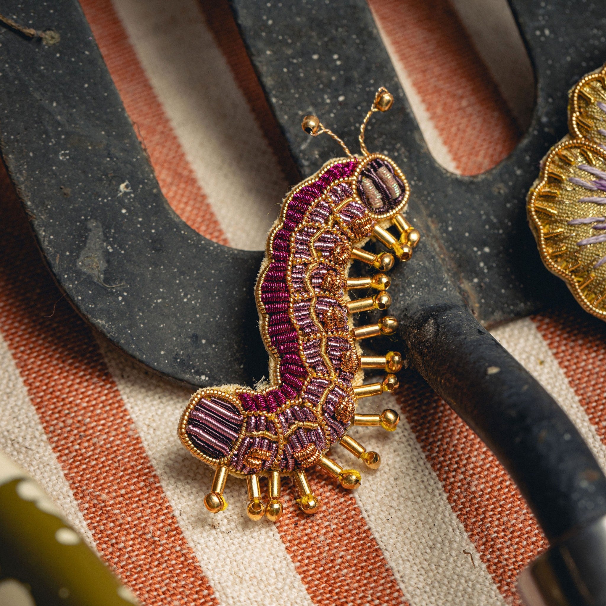Colette the Caterpillar Brooch - Brooch photographed on a gardening hand fork