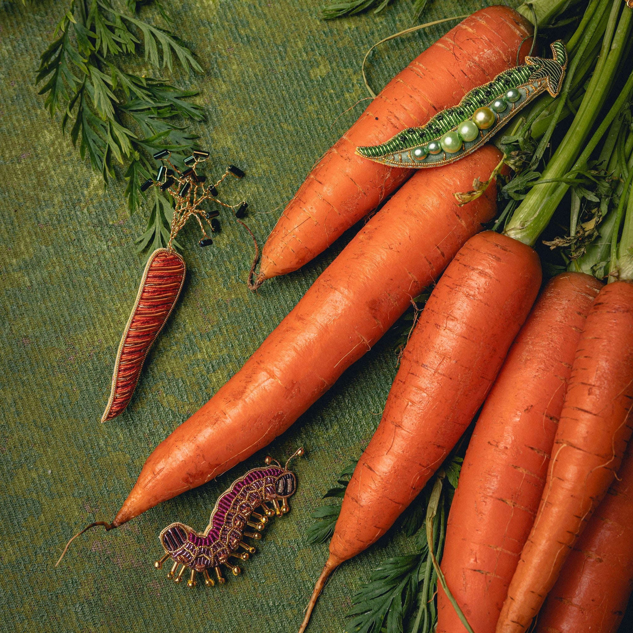 How Does Your Garden Grow? Collection of Hand Embroidered Jewellery - Embroidered brooches photographed with carrots on a green background 