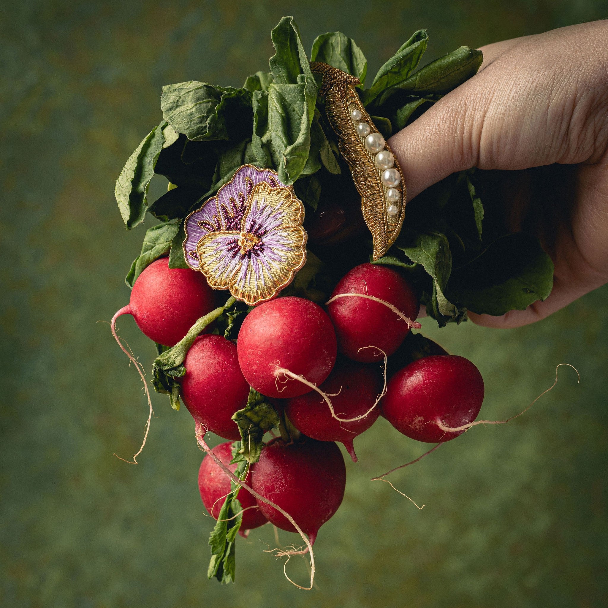 How Does Your Garden Grow? Collection of Hand Embroidered Jewellery - Hand holding a bunch of radishes with decorative brooches on a green background