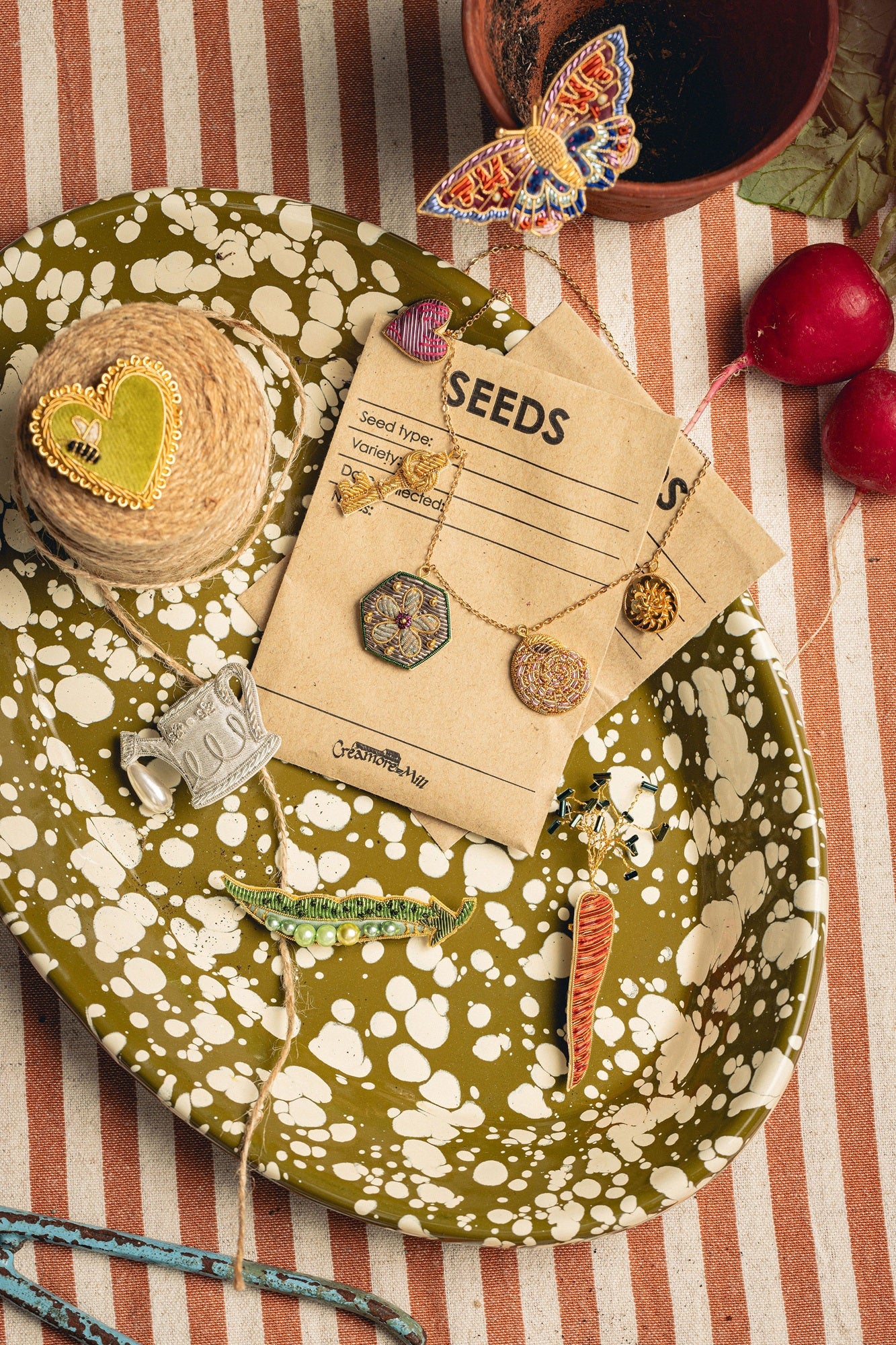 How Does Your Garden Grow? Collection of Hand Embroidered Jewellery - Jewellery on a decorative green plate, seed packets and a striped fabric background