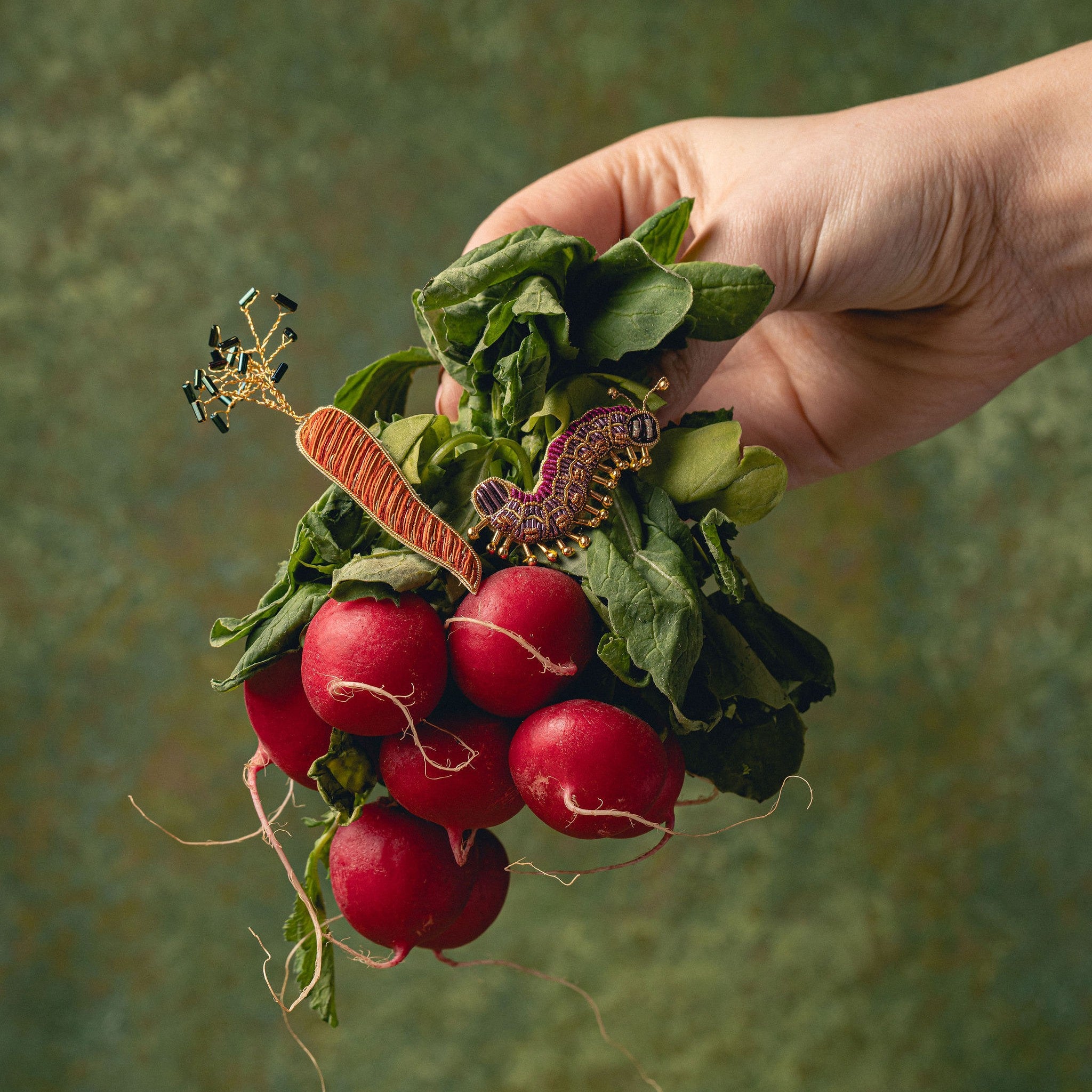 How Does Your Garden Grow? Collection of Hand Embroidered Jewellery - Hand holding a bunch of radishes against a green background