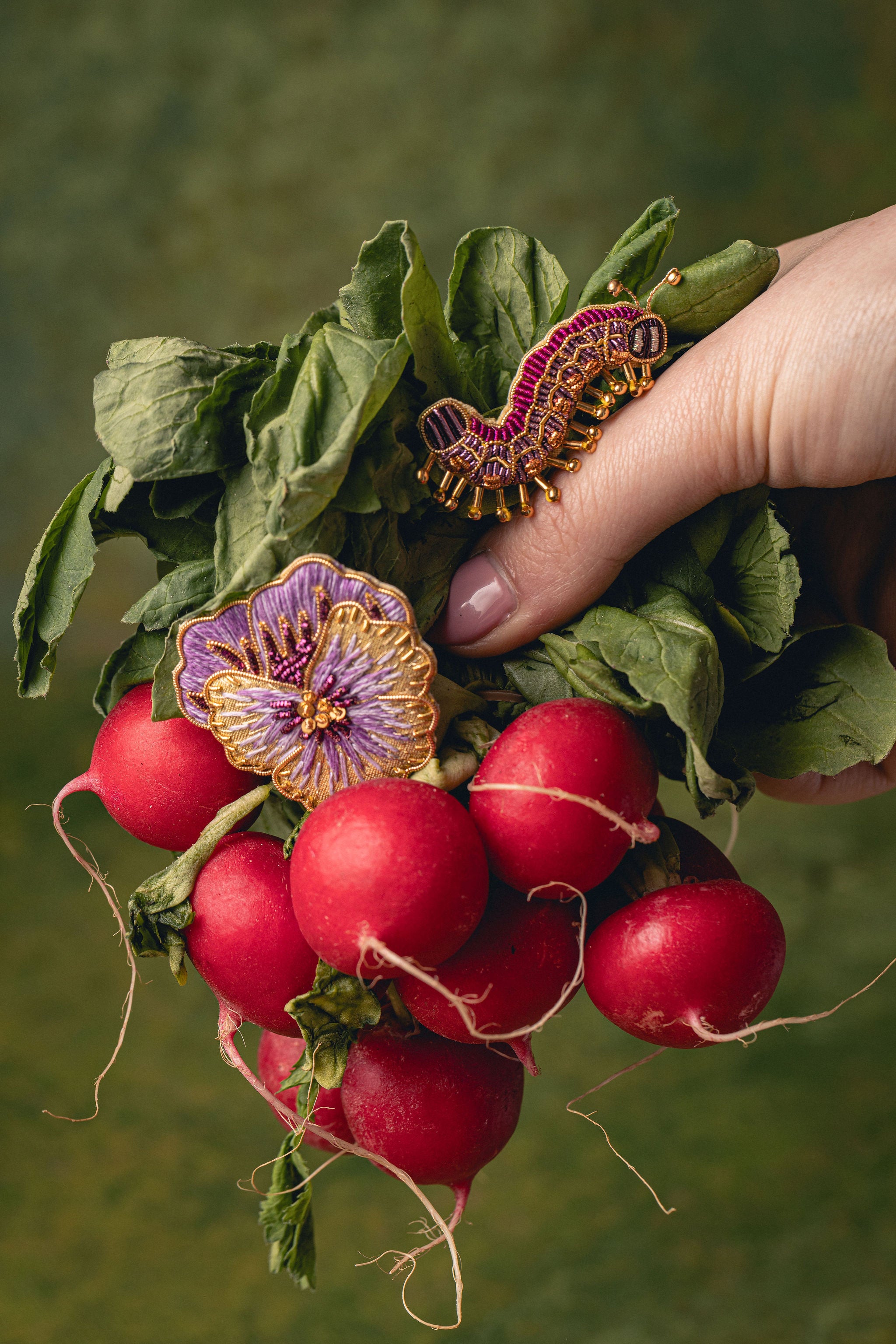 How Does Your Garden Grow? Collection of Hand Embroidered Jewellery - Hand holding radishes with decorative brooches on a green background