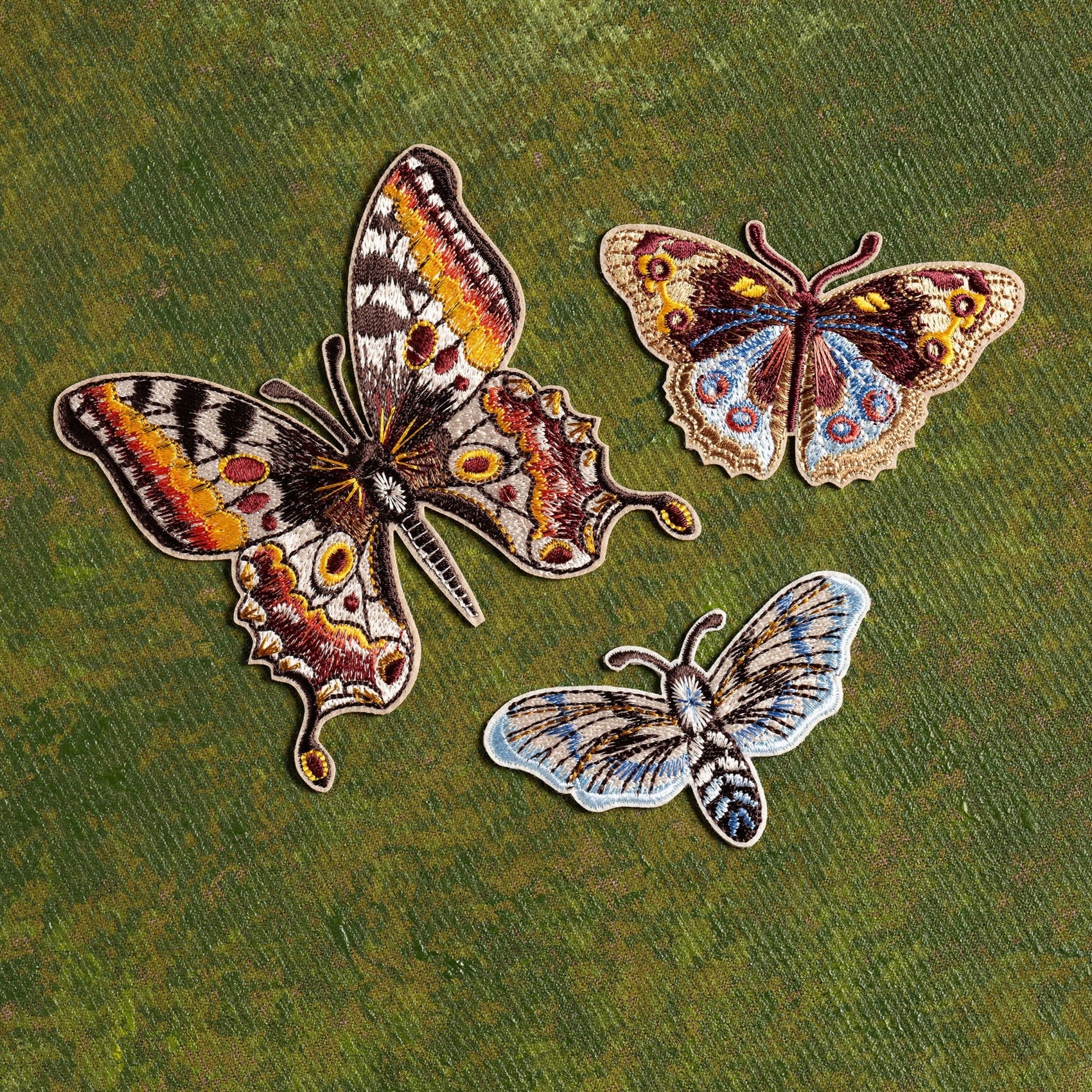 Kaleidoscope Butterflies Embroidered Patch Set - Three butterfly patches on a textured green background