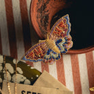 Kaleidoscope Butterfly Brooch - Hand Embroidered brooch photographed on a terracotta pot with a stripe background 