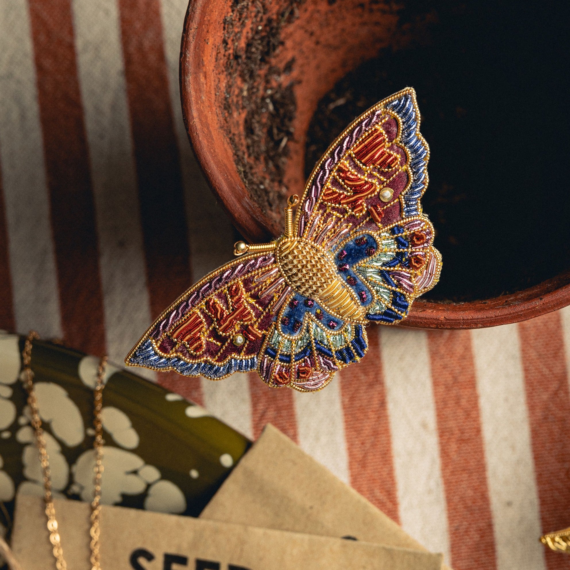 Kaleidoscope Butterfly Brooch - Hand Embroidered brooch photographed on a terracotta pot with a stripe background 