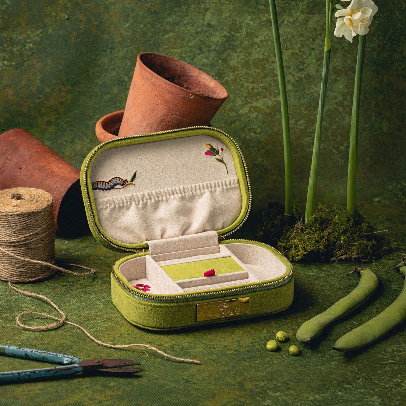 The Garden Embroidered Jewellery Box - Green jewellery box with embroidered interior on a green textured background with plants and gardening supplies